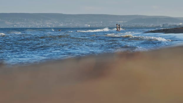 Sea waves washing sandy beach in Crimea with tourists enjoying summer vacation on a beautiful sunny day