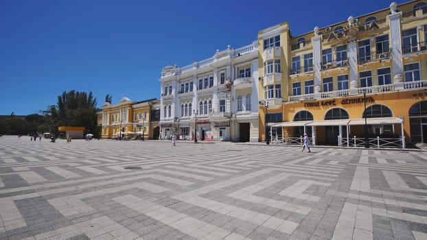 Tourists walking in Nakhimov Square with colorful buildings under blue sky in Sevastopol, Crimean peninsula