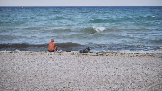 Retiree enjoying the peaceful atmosphere of the Crimean beach with his loyal companion, contemplating the mesmerizing sea waves