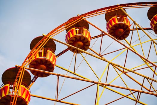Ferris wheel with yellow and red cabins rotating in amusement park under blue sky in Crimea