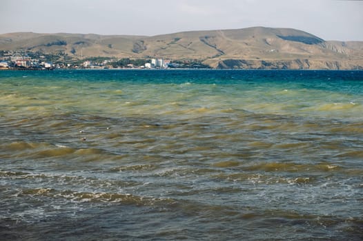 Koktebel bay waters showing signs of blooming algae with distant cityscape and bare mountains in Crimea, Russia