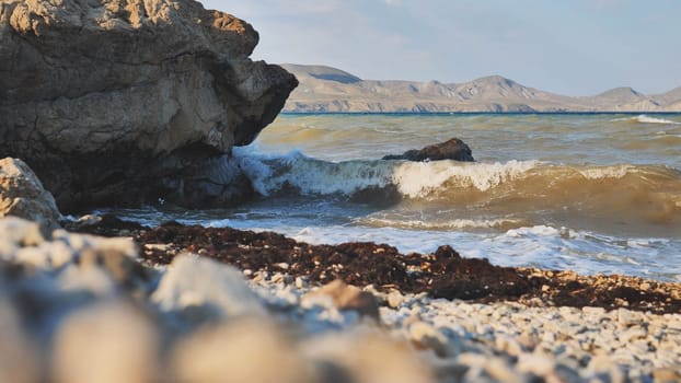 Scenic view of waves crashing on a rocky beach in Crimea, with mountains visible in the distance during a beautiful sunset