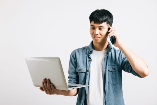 Portrait Asian smiling young man holding a laptop and talking on cell mobile phone studio shot isolated white background, Happy excited lifestyle businessman using computer and talking on smartphone