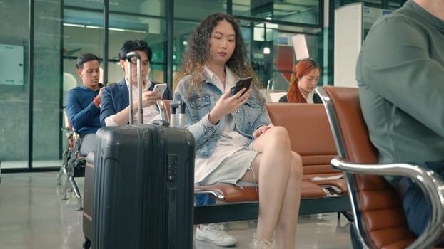 Passenger traveler woman in airport gate play smartphone for waiting air vacation travel, hipster female sitting and using mobile phone in terminal hall area while waiting for her traveling flight