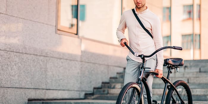 Way to office and modern worker in town. Sport, physical active and healthy lifestyle. Serious attractive millennial man hipster manager in stylish clothes carries bicycle on city stairs, free space