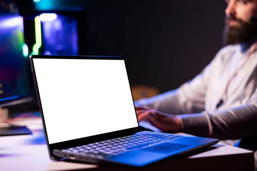 Close up of mockup laptop next to man playing videogames in front of subscribers during livestream, defeating enemies. Pro gamer streaming game, wearing headphones, using isolated screen notebook
