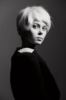 Captivating black and white image of a young woman with an elegant short blonde hairstyle. She is dressed in a sleek black outfit, thoughtful gaze directed towards the camera, embodying artistry and