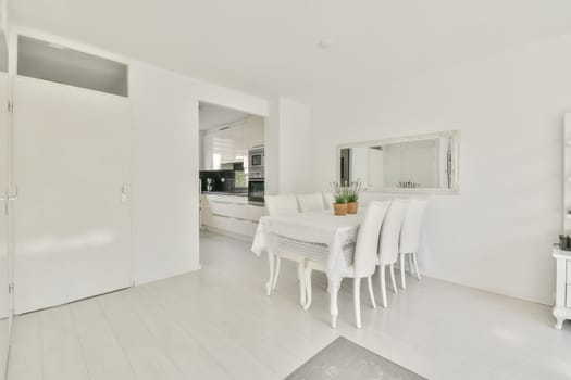 a white dining room with wooden flooring and large mirror on the wall above it is an open kitchen area