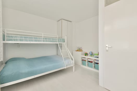 a children's room with bunks and storage space in the wall is white, there is a blue blanket on the bed