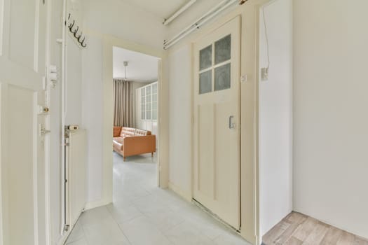 an empty hallway with white walls and wooden doors, leading to the living room on the left is a sofa