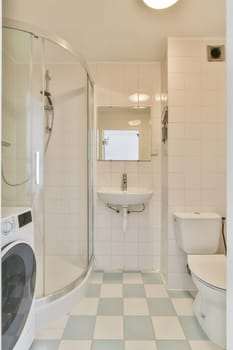 a white and blue tiled bathroom with a washer, toilet, and washing machine in the photo is taken