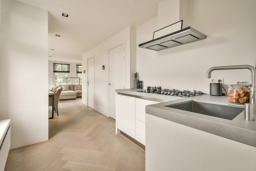 a modern kitchen with wood flooring and white cabinetry in the room is also furnished by an open - plan living area