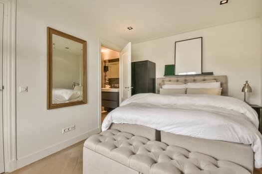 a bedroom with white walls and wood flooring the room has a large bed, a mirror on the wall