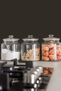 food in glass jars on a kitchen counter with uts and spoons next to the jar, which is filled with oats