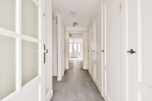 a long hallway with tile flooring and white trim on the walls, leading to an open door that leads to another room