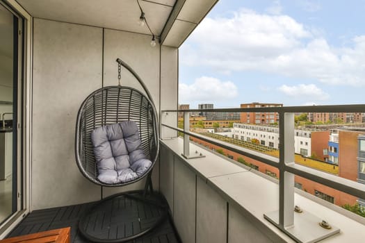 a balcony with a hanging chair on the left and a view of buildings in the back ground to the right