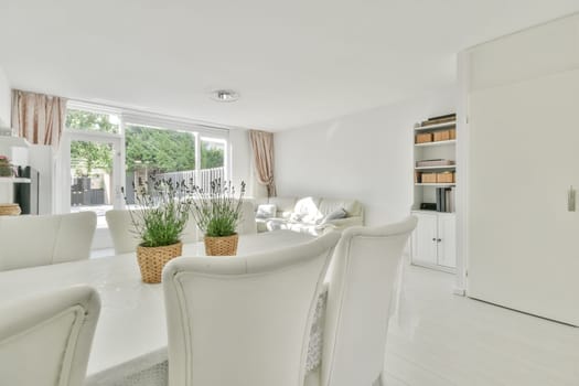 a living room with white furniture and an open door leading to the dining area, which is well lit by natural light