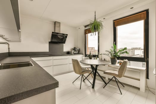 a kitchen and dining area in a modern apartment with white cabinets, black counter tops, and an open window overlooking the city