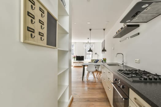a long narrow kitchen with white walls and wood flooring, along with black granite countertops on either sides