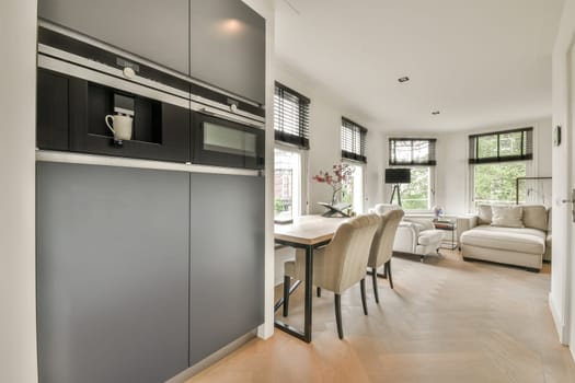 a kitchen and dining area in a modern home with white walls, hardwood flooring and dark grey cabinetry