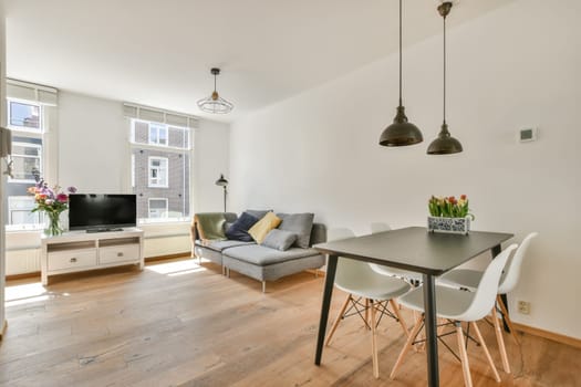 a living room with white walls and hardwood flooring, including a small dining table surrounded by two grey chairs
