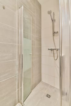 a bathroom with a shower stall and toilet roll on the left hand side, there is a white tiled wall
