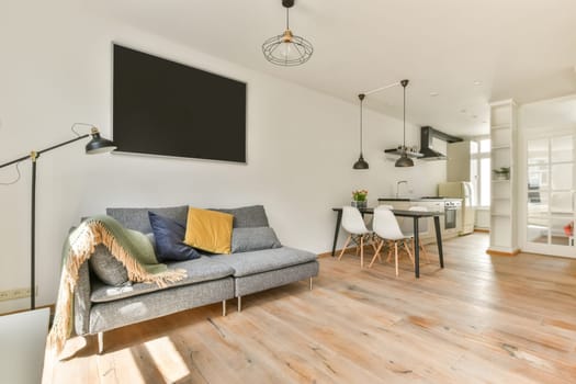 a living room with white walls and wood flooring the couch is grey, yellow and green pillows are on the sofa