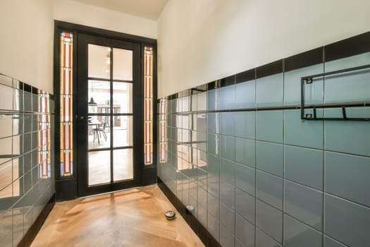 a hallway with glass doors and tiled walls on both sides, leading to an open door that leads into the dining area