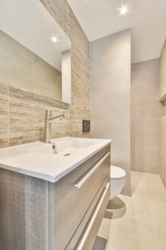 a modern bathroom with beige tile walls and white counters, along the wall is a large mirror above the sink