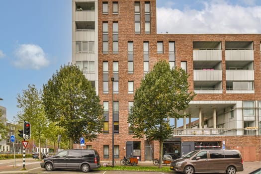 two cars parked in front of a tall brick building with balks on the side, and trees lining the street