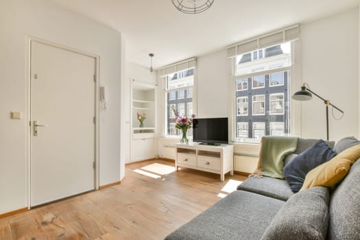 a living room with wood flooring and white walls, including a grey sofa and a tv on the wall