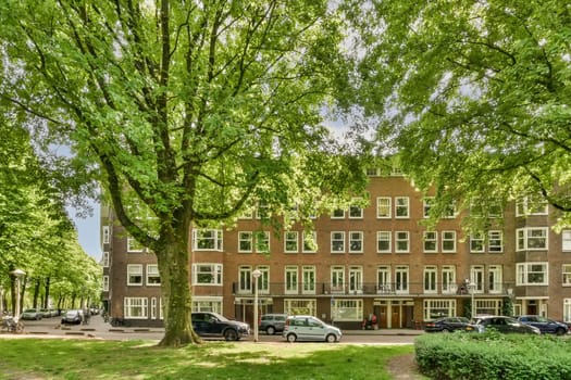 an apartment in the netherlands, with cars parked on the street and green trees lining the side of the building