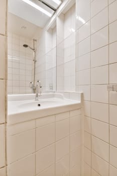 a bathroom with white tiles on the walls, and a mirror in the corner to the sink is next to it