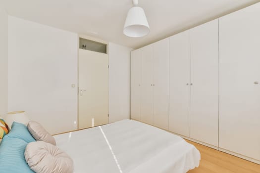 a bedroom with white walls and wood flooring the room has a bed, cabinetd cupboards and wardrobes