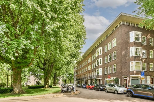 an apartment building with cars parked on the street and trees lining the side of the road in amsterdam, netherlands