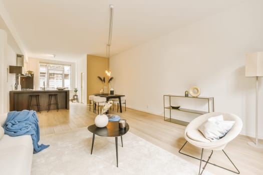 a living room with wood flooring and white couches in front of the sofa is an open kitchen area