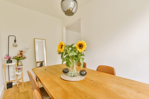 a dining room with sunflowers in a glass vase on the wooden table and two chairs at the wall is white