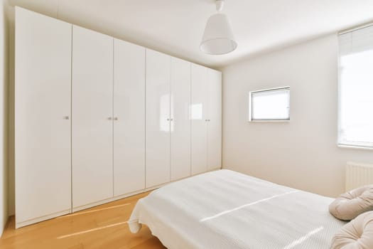 a clean white bedroom with wood flooring and built in wardrobes on the left side of the room, there is a window