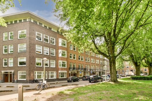 an apartment building with trees in the front and cars parked on the street next to each other bricked buildings