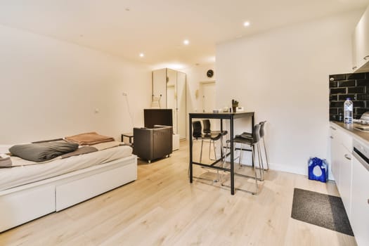 a living room with wood flooring and white walls, there is a small dining table in front of the couch