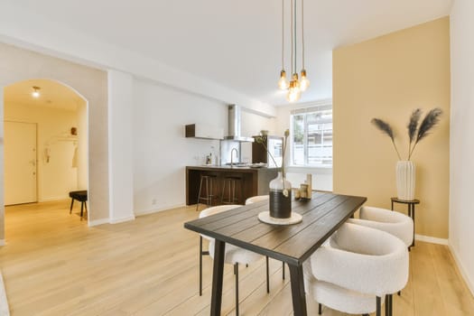 a dining room with wood flooring and an open kitchen area in the back wall to the room is white