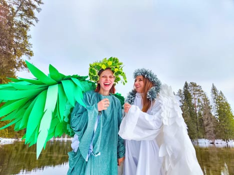 Two girls in elegant white and green dresses celebrate nature's beauty by a serene lake, embodying the seasonal transition.
