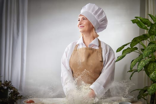 An elderly woman dressed as a cook joyfully tosses flour in the air while posing for a fun photo shoot in a warm kitchen environment.