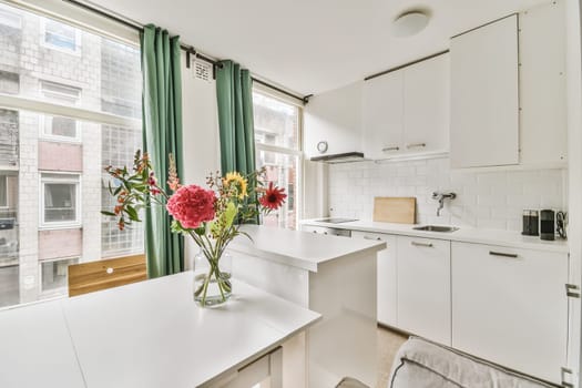 a white kitchen with flowers in the vase on the counter and window to the left, looking out onto the street