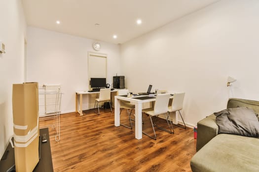 a living room with white walls and wood flooring, including a computer desk in the corner of the room