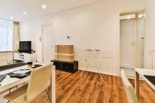 a living room with wood flooring and white walls, including a dining table and two chairs in front of the window