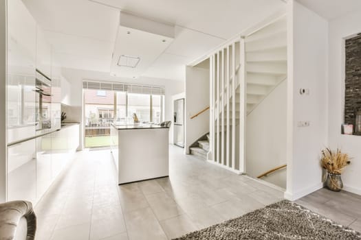 a living room with white walls and grey flooring in the center of the room is an open kitchen area