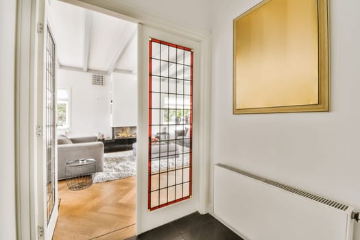 a living room with white walls and wood flooring, framed by a red glass paneled door that leads to the entryway