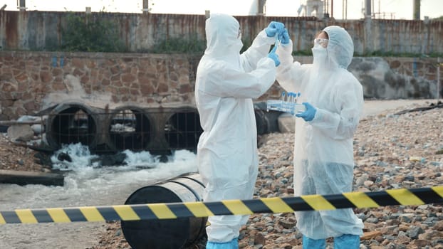 Ecologist sampling water from the river with test tube, Scientist or Biologist in a protective suit and protect mask collects sample of waste water from industrial for analyze, problem environment