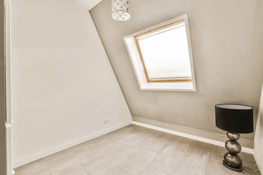 an empty room with a lamp on the floor and a small window in the corner to the other room is visible